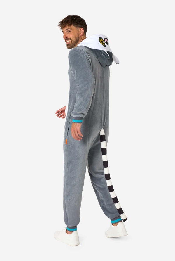 Een man draagt ​​een grijze en witte maki onesie voor volwassenen met speelse capuchondetails en gezellig, zacht materiaal, perfect voor loungen of verkleedevenementen. Inclusief zwart-witte staart. Volledig lichaamsbeeld vanaf de zijkant.