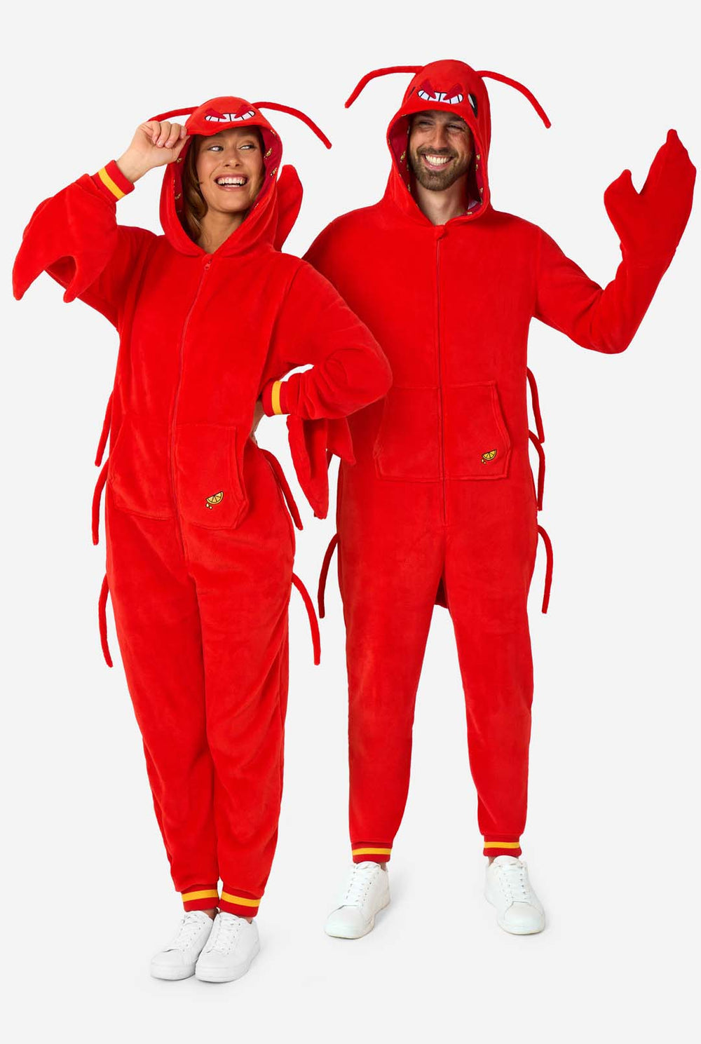 Een man en een vrouw dragen een felrode onesie voor volwassenen met kreeftenthema, speelse capuchondetails en knus, zacht materiaal, perfect om in te loungen of als verkleedkleding. Beiden dragen hun capuchon op hun hoofd.
