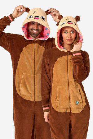 Een lachende man en een vrouw dragen een bruine onesie voor volwassenen met de afbeelding van een otter. De onesie heeft een capuchon met oren, een schattig gezichtje en speelse otterdetails, perfect voor een gezellig loungen of verkleedpartijtje.
