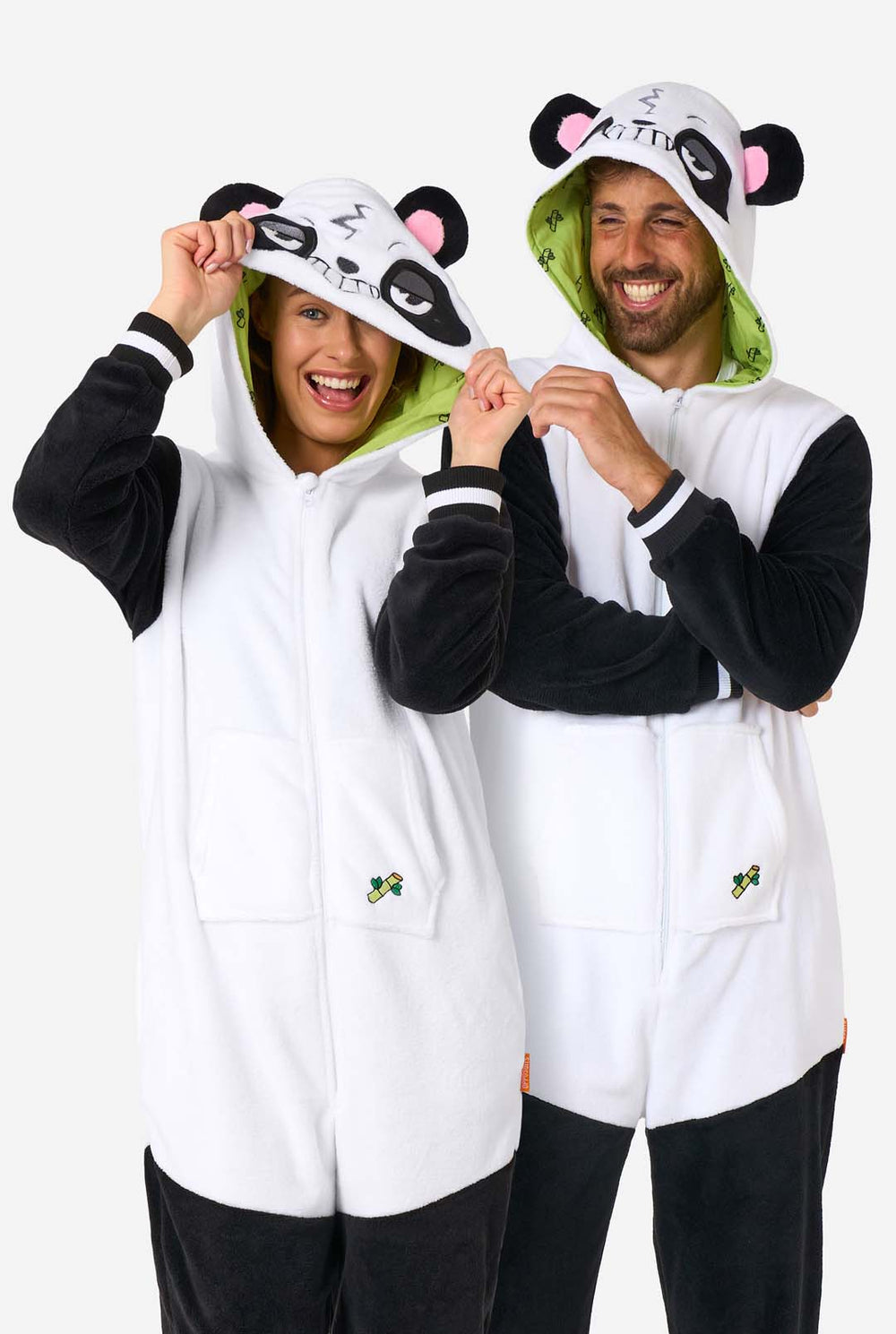 Een man en een vrouw dragen een onesie voor volwassenen met een pandathema. Deze comfortabele onesie is uitgevoerd in zwart-witte pandakleuren en heeft een speelse capuchon met panda-oren en een schattig gezichtje. Perfect om in te loungen of voor een leuk verkleedfeestje.