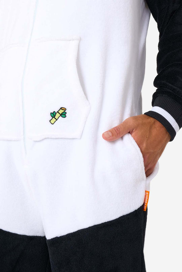 Een man draagt ​​een volwassen onesie met panda-thema. Deze gezellige onesie heeft de zwart-witte pandakleuren met een speelse capuchon met panda-oren en een schattig gezichtje. Perfect voor loungen of leuke verkleedgelegenheden. Close-up van de zak.