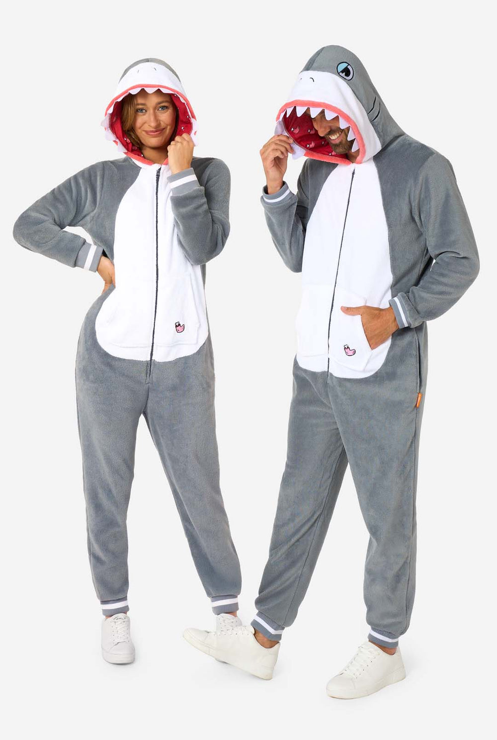 Een man en een vrouw dragen een grijs met witte haai onesie voor volwassenen met speelse details in de capuchon en knus, zacht materiaal, perfect voor loungen of verkleedpartijen. Beiden dragen hun capuchon op hun hoofd.