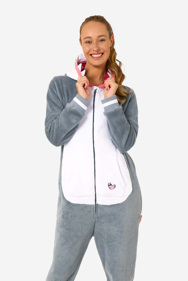 Een vrouw draagt een grijs met witte haai onesie voor volwassenen met speelse details in de capuchon en knus, zacht materiaal, perfect voor loungen of verkleedpartijen. Ze heeft haar capuchon op haar rug