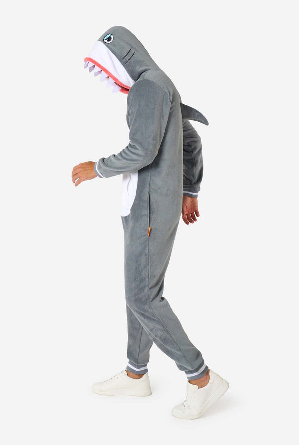 Een man draagt ​​een grijze en witte haaienonesie voor volwassenen met speelse capuchondetails en gezellig, zacht materiaal, perfect voor loungen of verkleedevenementen.  Volledig lichaamsbeeld vanaf de zijkant.
