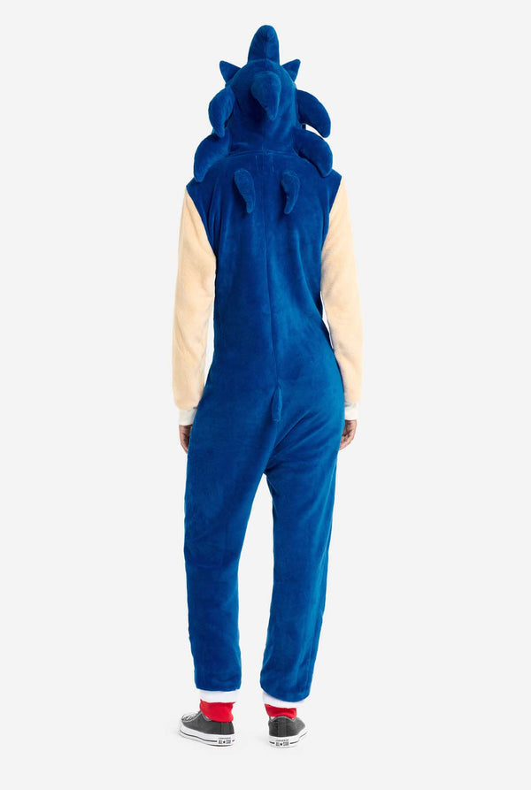 Een vrouw is gekleed in een gezellige, blauwe Sonic the Hedgehog onesie voor volwassenen, met zachtbeige patches op de voorkant en mouwen om de iconische look van Sonic na te bootsen. De onesie heeft een capuchon ontworpen met het herkenbare gezicht van Sonic. De ritssluiting aan de voorkant zorgt voor een comfortabele pasvorm. Haar uitdrukking is kalm en ontspannen. Zicht vanaf de achterkant.