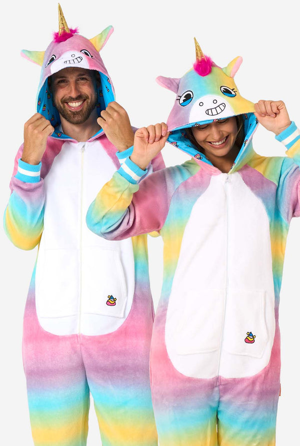 Een man en vrouw dragen een kleurrijke onesie voor volwassenen ontworpen als een regenboog eenhoorn. De onesie heeft een levendig verloop van pastelkleuren, een gouden hoorn en speelse eenhoorndetails, perfect voor gezellig loungen of verkleedfeestjes. De mannen en vrouwen hebben allebei hun capuchon op.