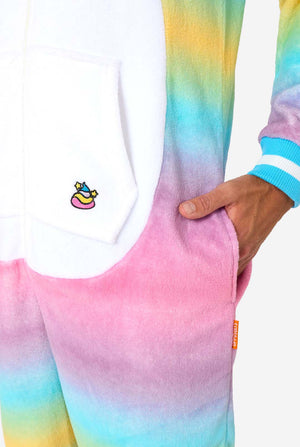 Een man draagt ​​een kleurrijke volwassen onesie ontworpen als een regenboogeenhoorn. De onesie heeft een levendig verloop van pastelkleuren, een gouden hoorn en speelse eenhoorndetails. Zakje met close-upafbeelding.