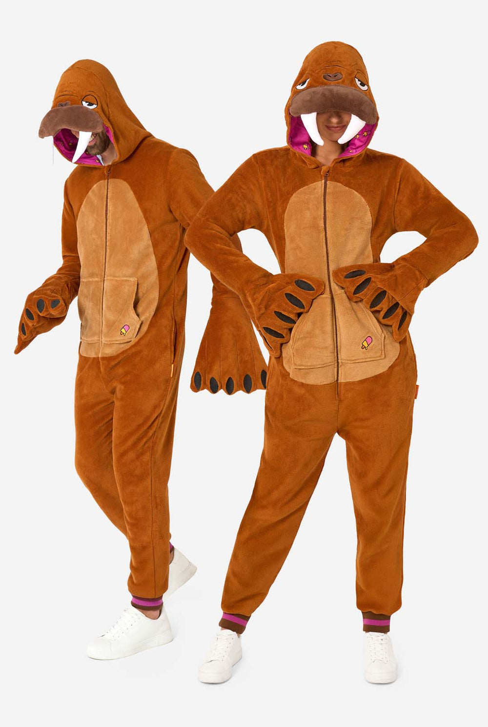 Een vrolijke man en vrouw dragen een bruine onesie voor volwassenen die is ontworpen als walrus. De onesie heeft een capuchon met hoektanden, opgestikte handschoenen die op poten lijken en speelse walrusdetails, perfect voor gezellig loungen of verkleed feestjes. De capuchon zit op hun hoofd.