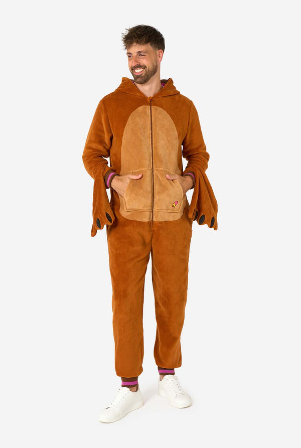 Een vrolijke man in een bruine volwassen onesie uitgevoerd in de vorm van een walrus. De onesie heeft een capuchon met hoektanden, gestikte handschoenen die op poten lijken en speelse walrusdetails, perfect voor gezellig loungen of verkleedfeestjes. Volledig lichaamsbeeld en de man die zijn hand in zijn zakken houdt.