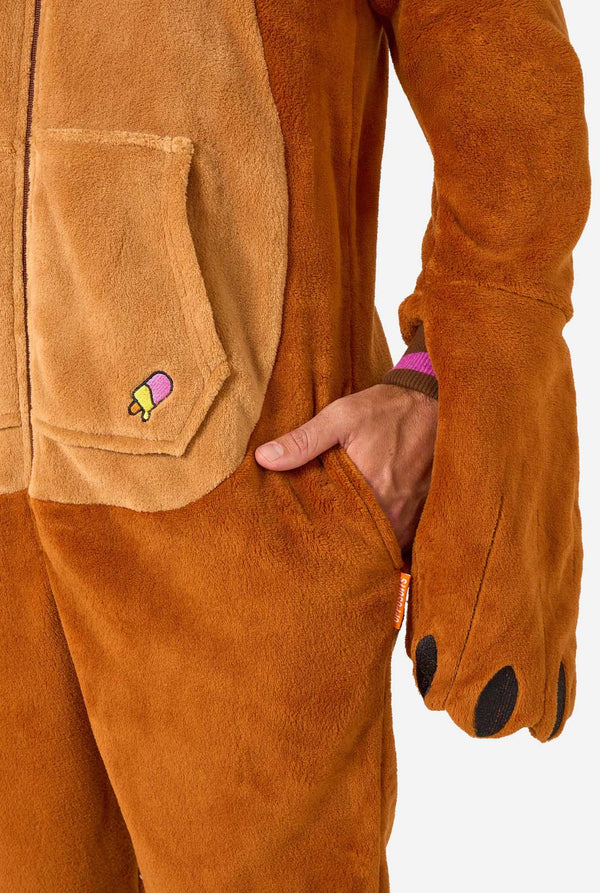 Een man in een bruine volwassen onesie uitgevoerd in de vorm van een walrus. De onesie heeft een capuchon met hoektanden, gestikte handschoenen die op poten lijken en speelse walrusdetails, perfect voor gezellig loungen of verkleedfeestjes. Zak van dichtbij.