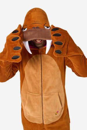 Een vrolijke man in een bruine volwassen onesie uitgevoerd in de vorm van een walrus. De onesie heeft een capuchon met hoektanden, gestikte handschoenen die op poten lijken en speelse walrusdetails, perfect voor gezellig loungen of verkleedfeestjes. Bovenlichaam close-up.