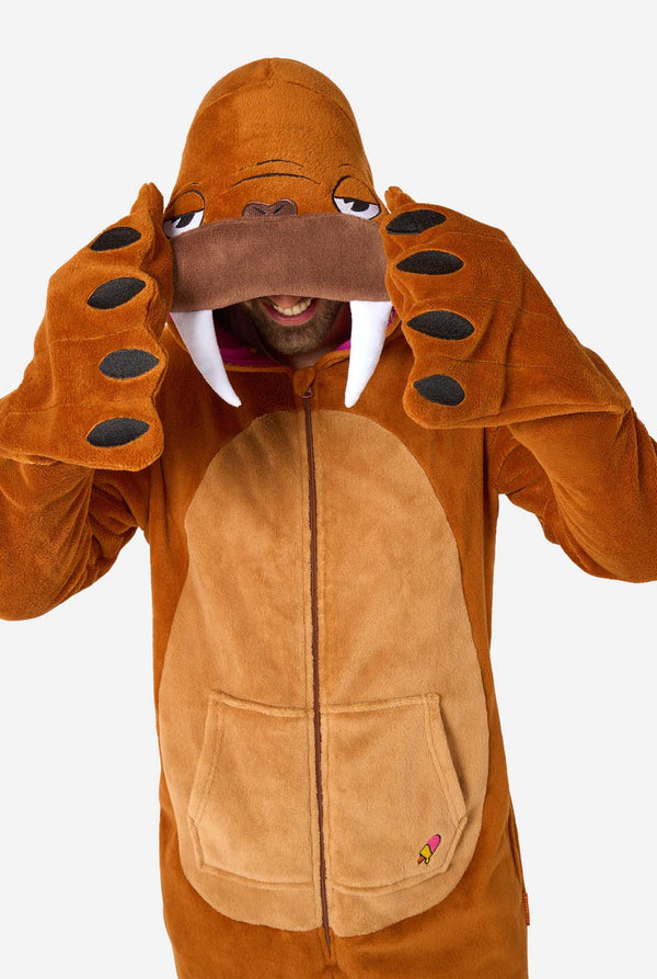 Een vrolijke man in een bruine volwassen onesie uitgevoerd in de vorm van een walrus. De onesie heeft een capuchon met hoektanden, gestikte handschoenen die op poten lijken en speelse walrusdetails, perfect voor gezellig loungen of verkleedfeestjes. Bovenlichaam close-up.