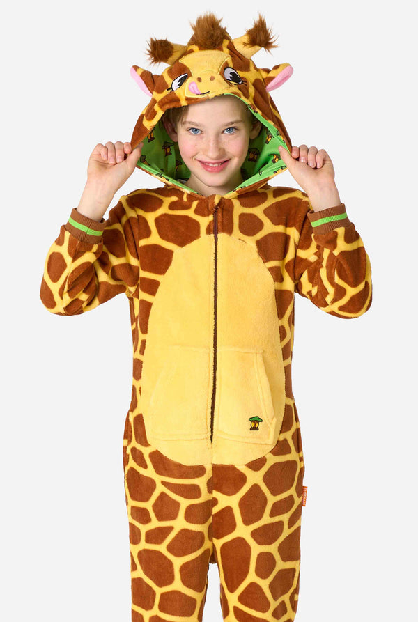 Een lachend kind draagt ​​een bruin-gele kinderonesie ontworpen als een giraffe. De onesie heeft een capuchon die lijkt op een giraffenkop.