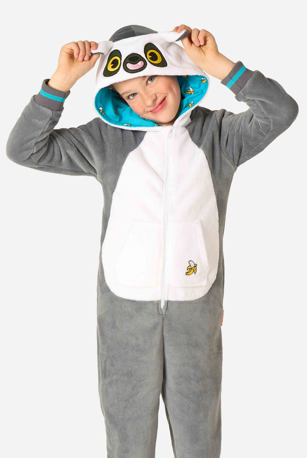 Een kind draagt ​​een comfortabel unisex kinderonesie in de vorm van een maki. De stof is gemaakt van grijs en wit pluche, heeft een capuchon met een cartoonmakigezicht en -oren en een speelse bananenprint op de zak. 