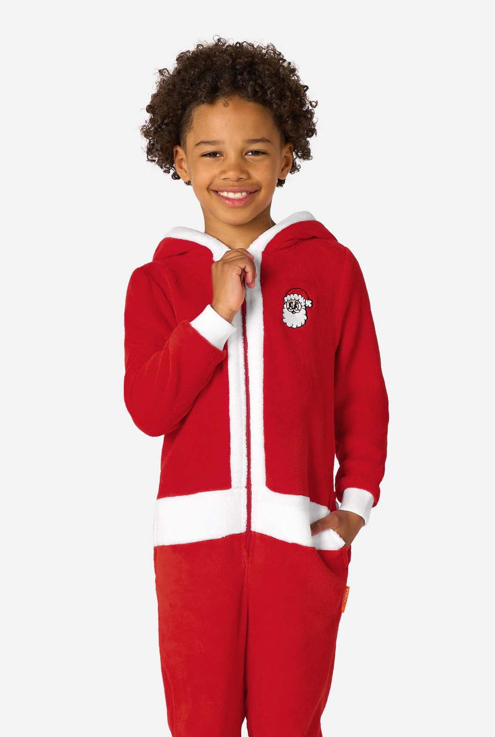 Kind dat een rode Santa-onesie met een wit afgewerkte capuchon draagt, iets zijwaarts staand met de handen in de zakken.