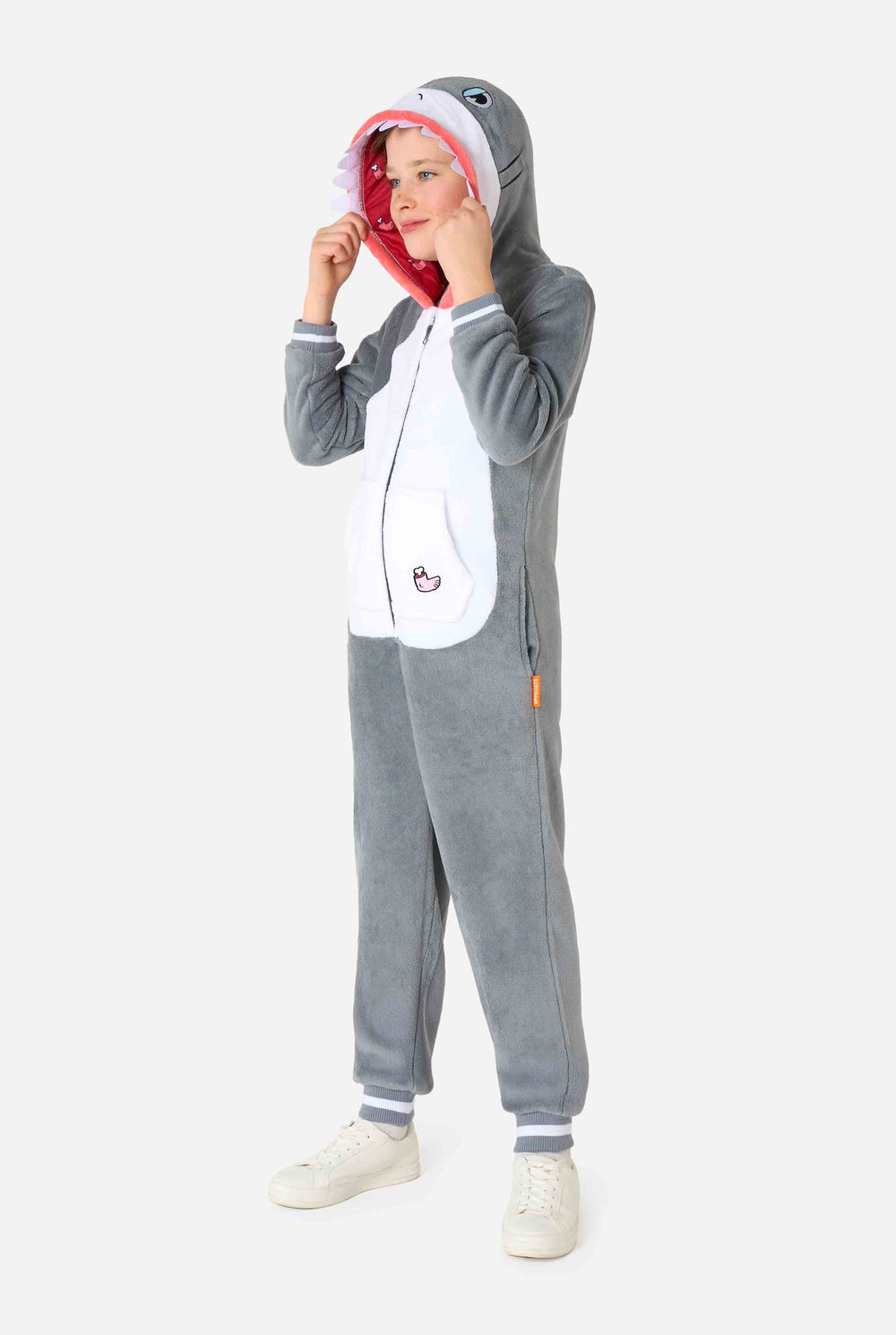 Een kind draagt ​​een grijze en witte kinderonesie met een haai, speelse capuchondetails en gezellig, zacht materiaal, perfect voor loungen of verkleedevenementen.