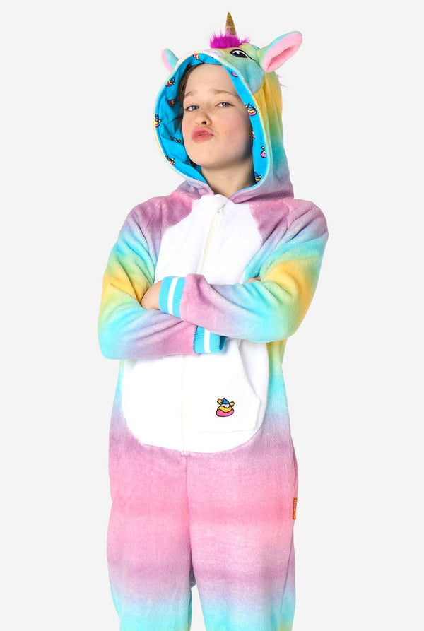 Een lachend kind draagt ​​een witte, roze, blauwe en gele kinderonesie ontworpen als eenhoorn. De Unicorn onesie heeft een capuchon die lijkt op een eenhoornkop en andere speelse details