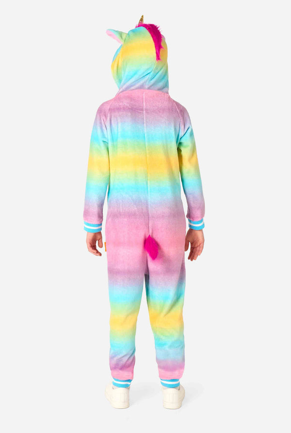 A smiling kid is wearing a white, pink, blue and yellow kids onesie designed as a unicorn. The Unicorn onesie features a hood resembling a unicorn head and other playfull details. View from the back, full body.