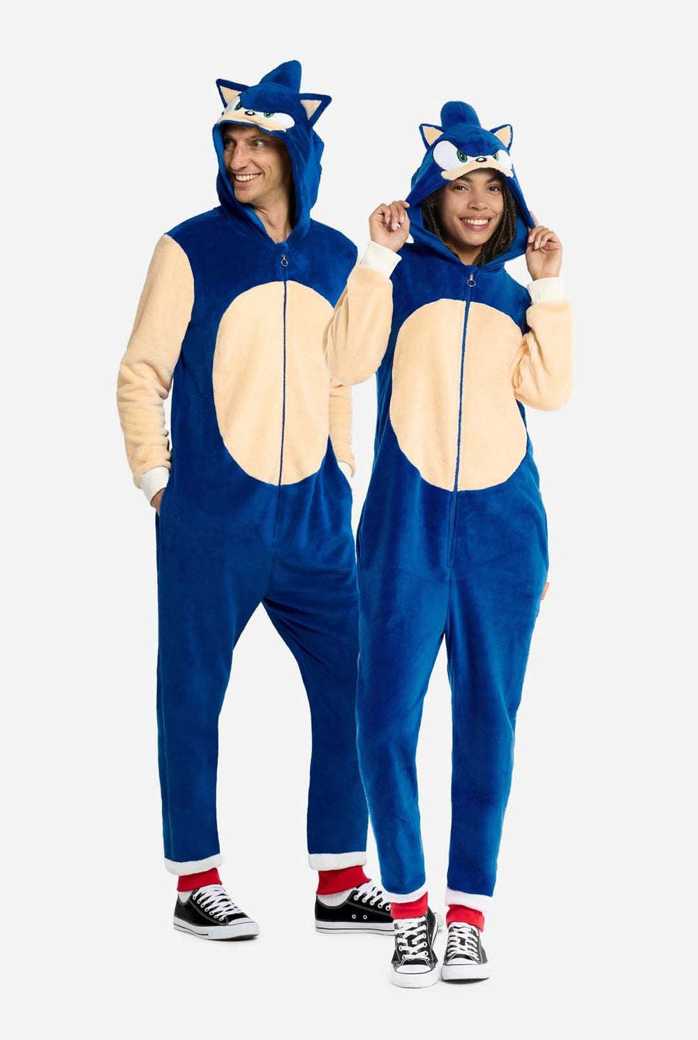 Een man en een vrouw dragen een speelse blauw-beige onesie voor volwassenen met Sonic the Hedgehog-thema van OppoSuits. De comfortabele onesie heeft een ritssluiting aan de voorkant en een capuchon die is ontworpen om te lijken op Sonics iconische gezicht, compleet met oren en een expressieve blik. De blauwe romp van het pak contrasteert met een beige buik, wat Sonics klassieke look nabootst.