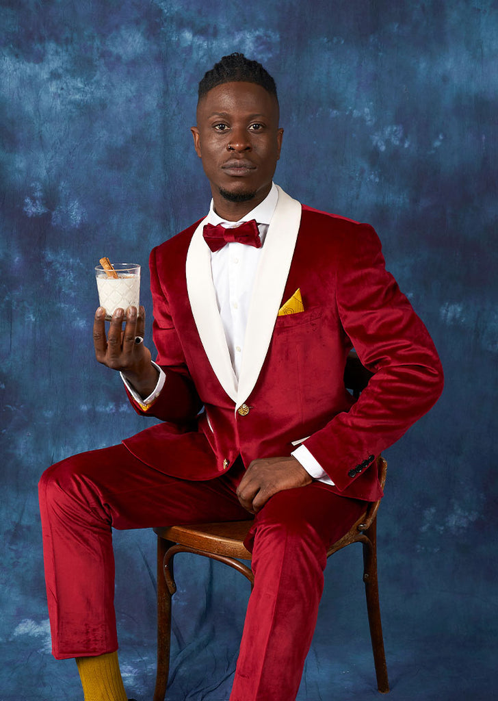 Man wearing Velvet Vibes red tuxedo, sitting on chair