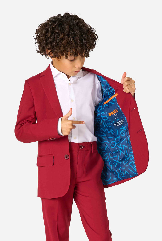 Een kind in een stijlvol bordeauxrood pak met een wit overhemd, dat er zelfverzekerd uitziet. De perfecte formele outfit voor speciale gelegenheden, bruiloften en feestjes voor jongens. Houd een kant van het jasje open.