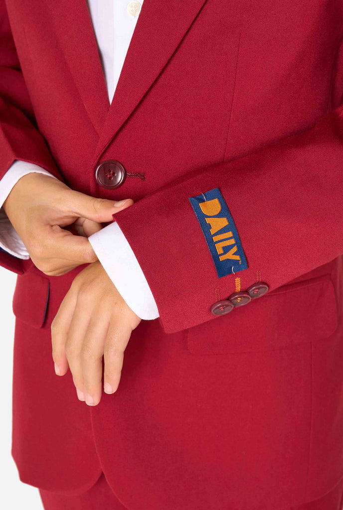 Een kind in een stijlvol bordeauxrood pak met een wit overhemd, dat er zelfverzekerd uitziet. De perfecte formele outfit voor speciale gelegenheden, bruiloften en feestjes voor jongens. Close up van de mouwen.