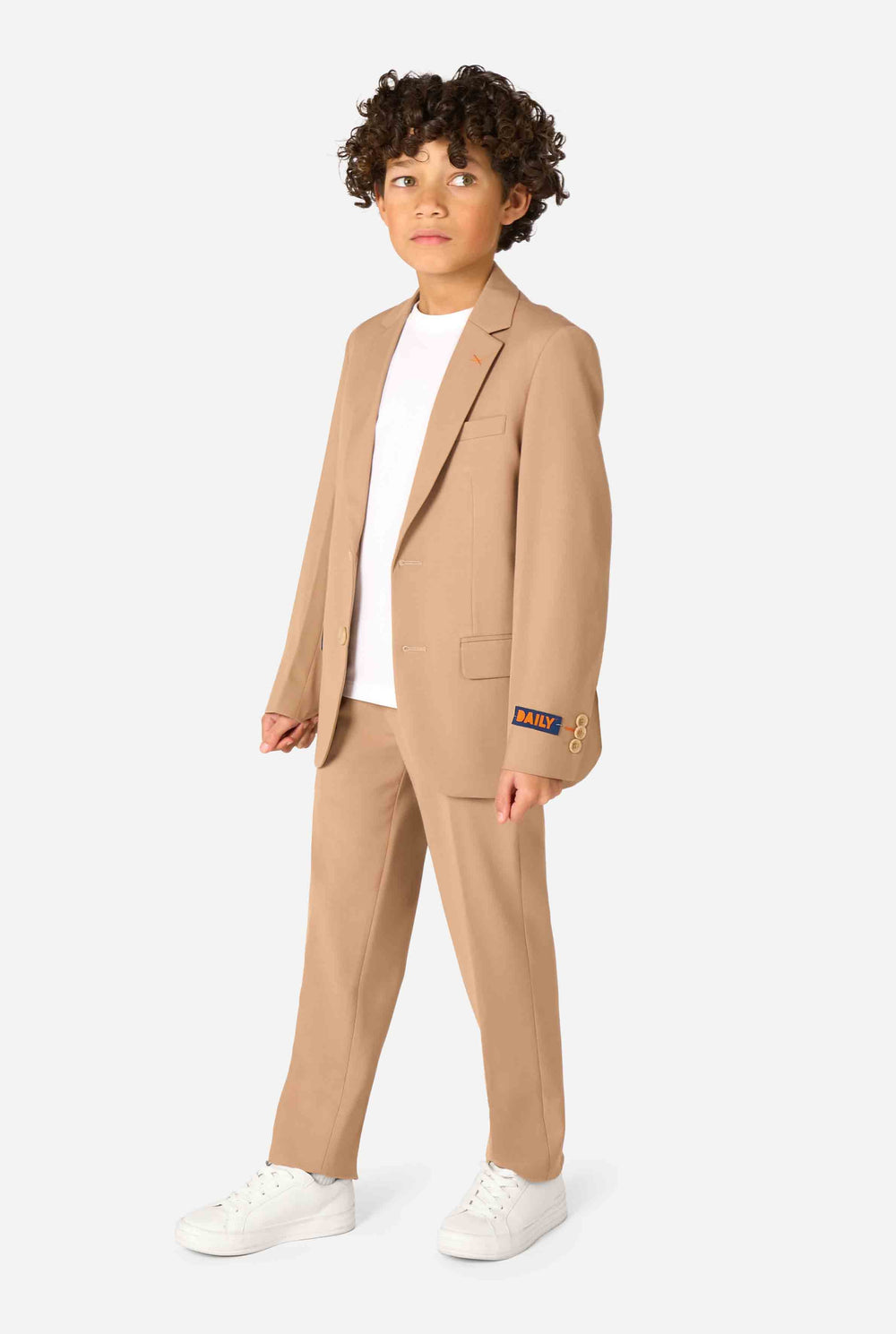 Een kind in een stijlvol lichtbruin/beige pak met een wit overhemd, wegkijkend van de camera. Perfecte formele outfit voor speciale gelegenheden, bruiloften en feestjes voor jongens.