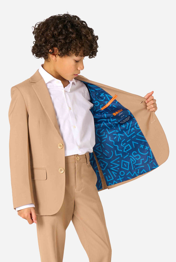 Een kind in een stijlvol lichtbruin/beige pak met een wit overhemd, wegkijkend van de camera. Perfecte formele outfit voor speciale gelegenheden, bruiloften en feestjes voor jongens. Houd een kant van het jasje open.