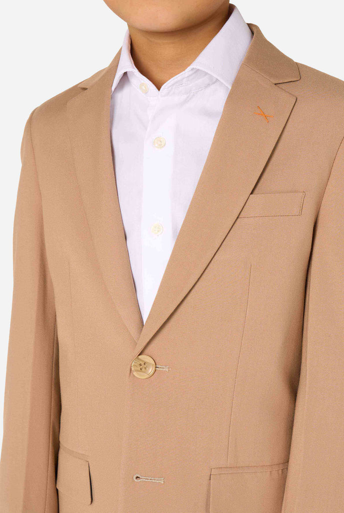 Een kind in een stijlvol lichtbruin/beige pak met een wit overhemd, wegkijkend van de camera. Perfecte formele outfit voor speciale gelegenheden, bruiloften en feestjes voor jongens. Close up van de borst.