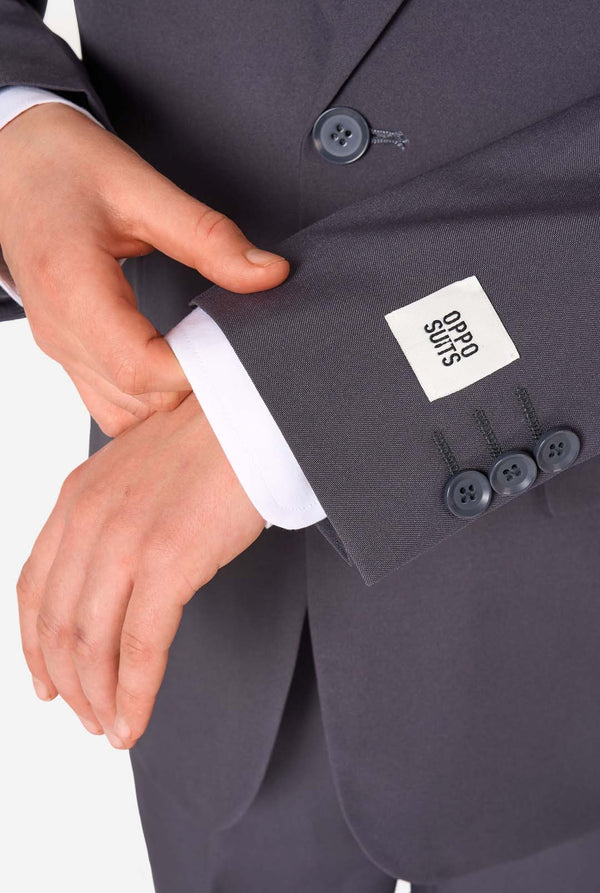 Een tienerjongen in een stijlvol antracietgrijs pak met een wit overhemd, vol zelfvertrouwen lachend. De perfecte formele outfit voor speciale gelegenheden, bruiloften en feestjes.