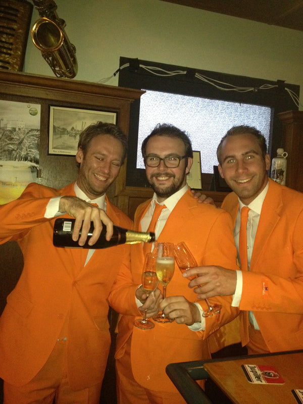 Een afbeelding van de 3 oprichters van Opposuits, gekleed in een oranje pak, champagne drinkend.