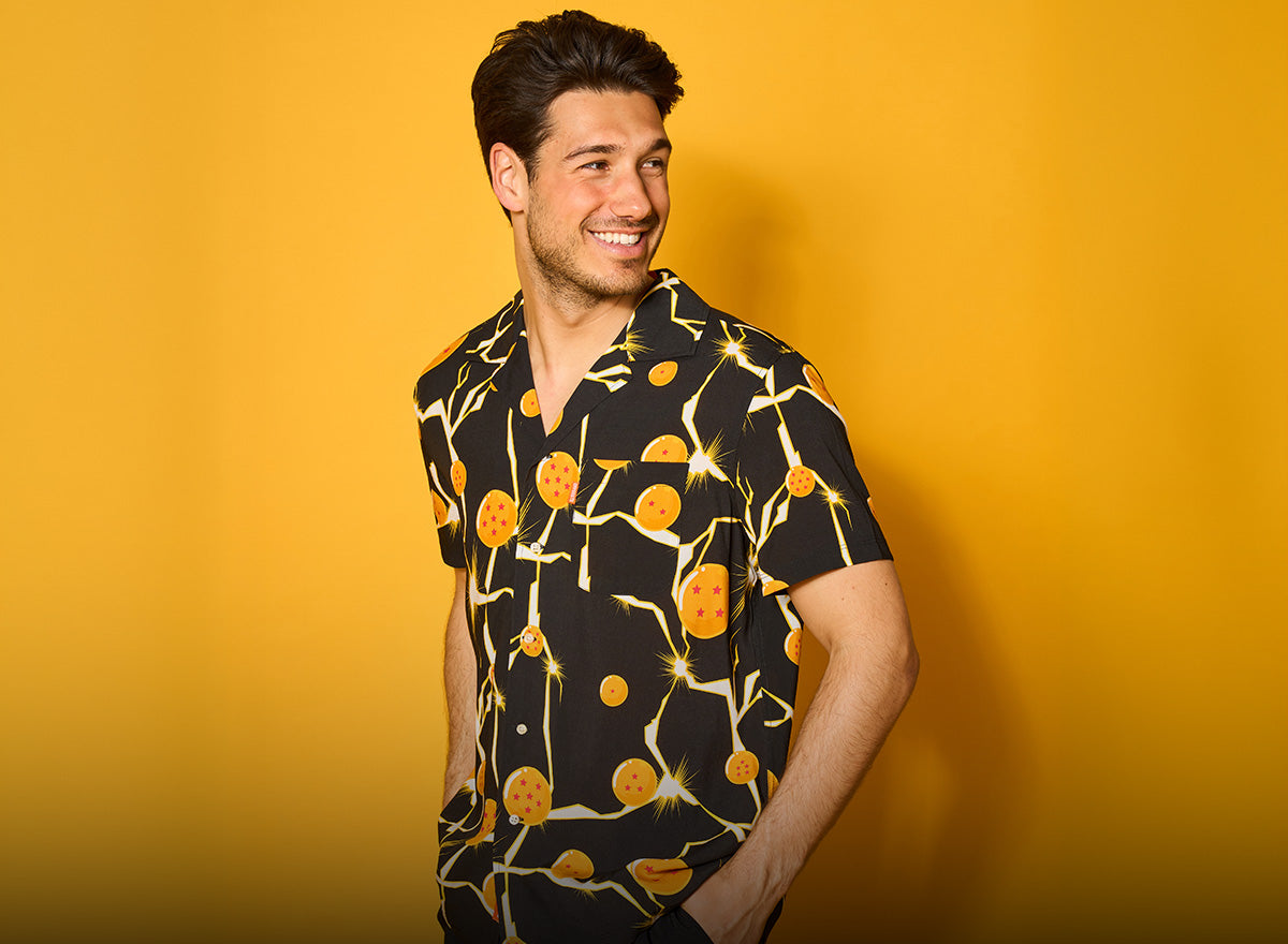 Smiling man in a black short-sleeve shirt printed with orange Dragon Balls and white lightning bolts, against a yellow backdrop.
