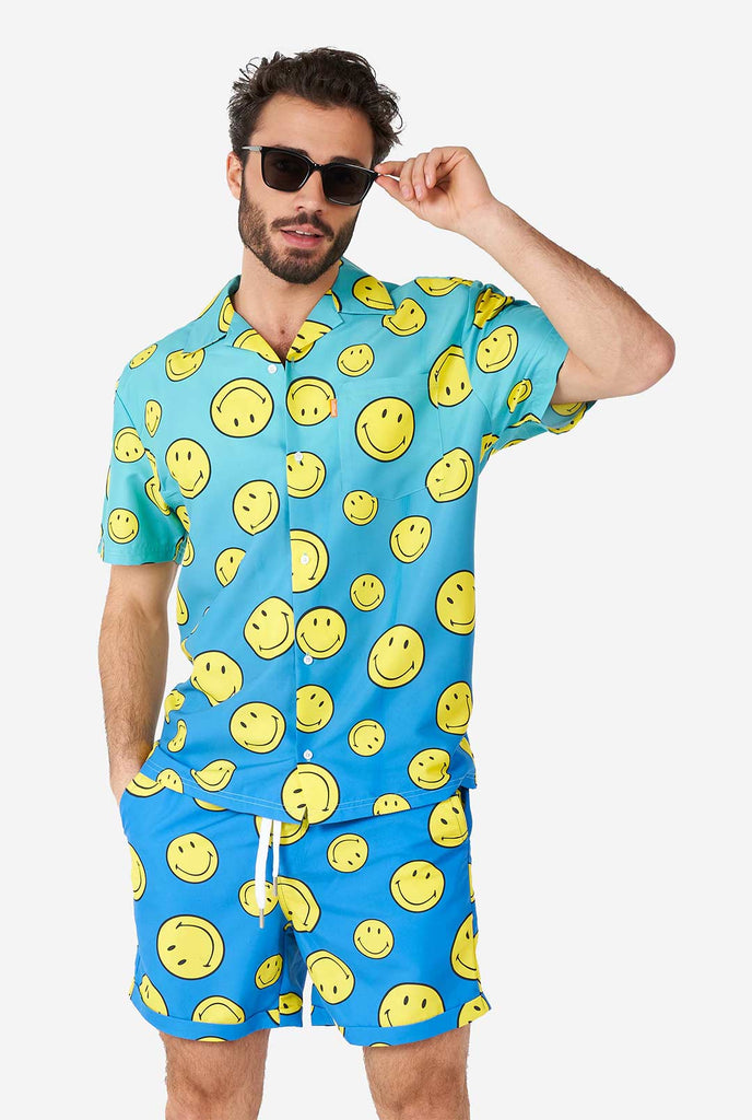 Man draagt ​​een blauwe zomerset, bestaande uit shorts en shirt, met smiley print