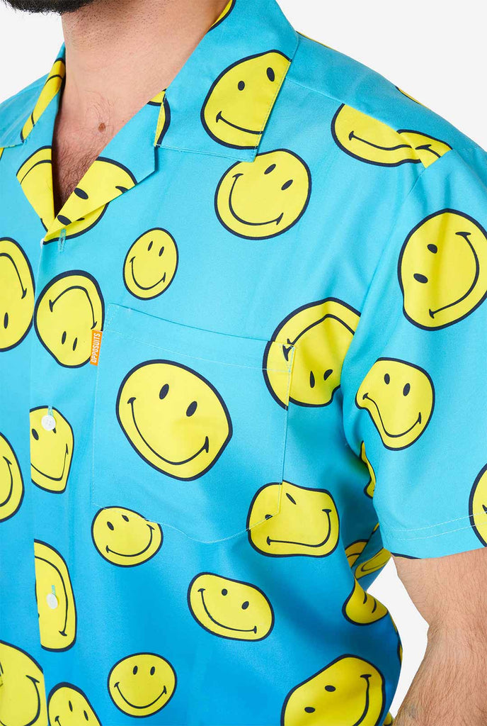 Man draagt ​​een blauwe zomerset, bestaande uit shorts en shirt, met smileyprint, shirt van dichtbij